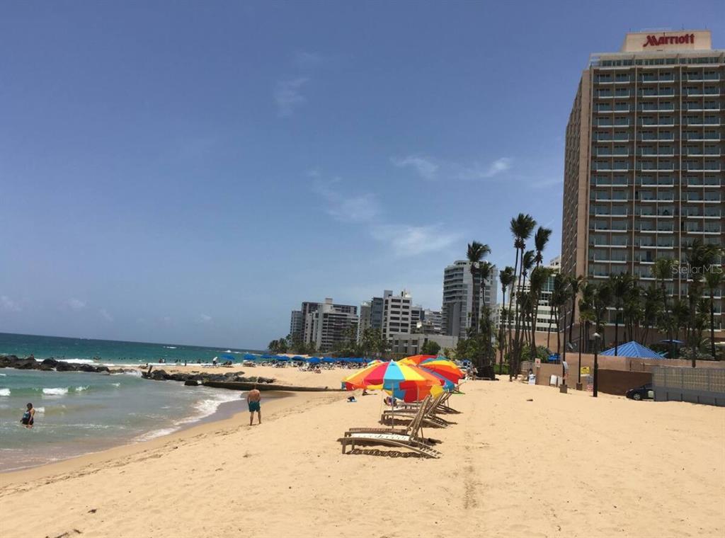 A sandy beach with lounge chairs and umbrellas in front of a tall Marriott hotel — 60 Caribe COND. CASTILLO UNIT 3B, SAN JUAN, PR
