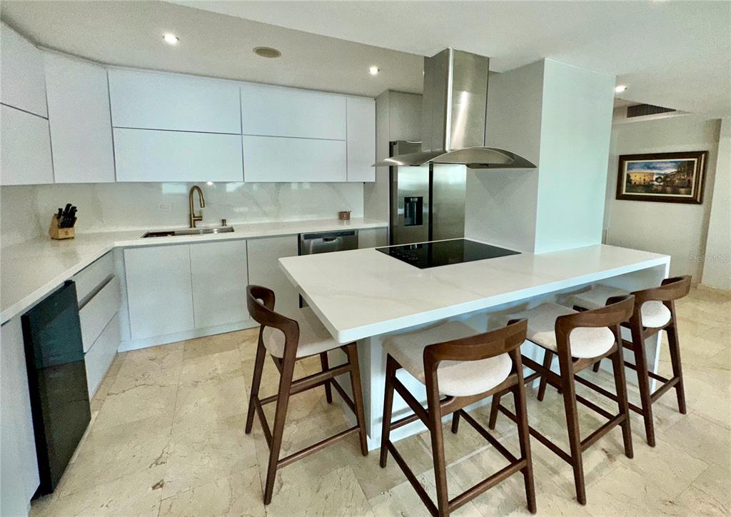 A modern kitchen features white cabinetry, a marble-topped island with bar stools, and stainless appliances — 60 Caribe COND. CASTILLO UNIT 3B, SAN JUAN, PR
