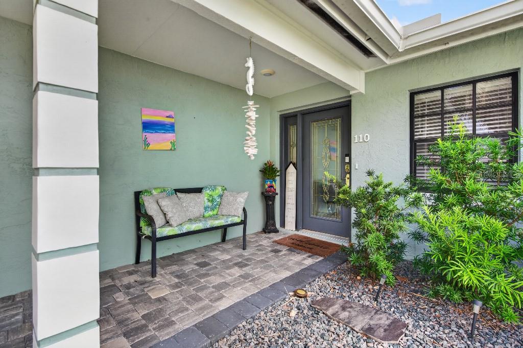 A covered front porch features a paved floor, a bench with patterned cushions, and a door — 110 CIMMARON DRIVE, PALM COAST, FL