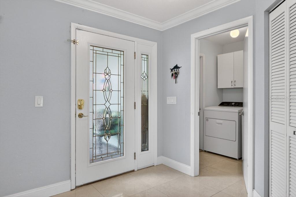 An entryway with a glass-paneled front door, light-colored tile flooring, and a laundry room visible — 110 CIMMARON DRIVE, PALM COAST, FL