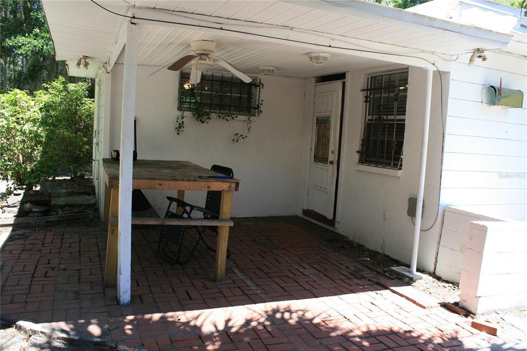 A covered brick patio features a wooden table, a ceiling fan, and a white door — 1822 NW 6TH AVENUE, GAINESVILLE, FL