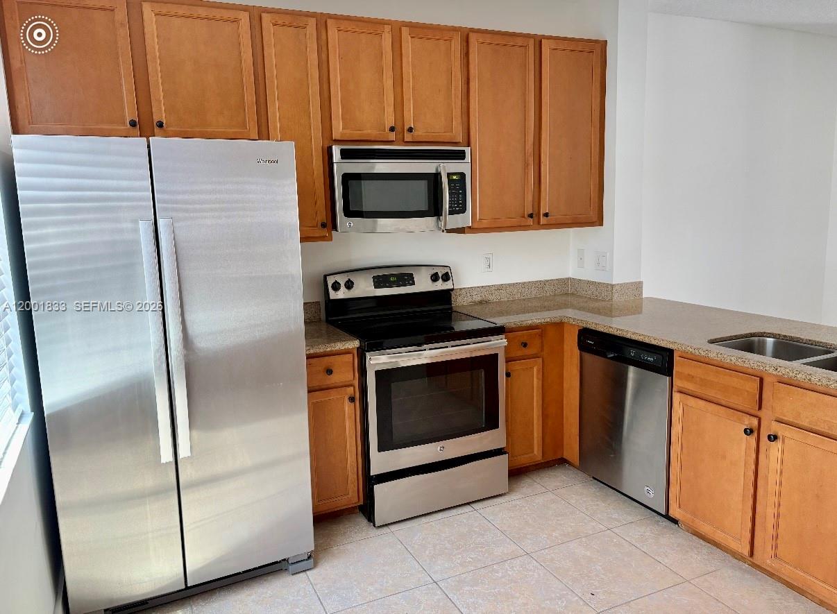A kitchen features wooden cabinets, granite countertops, stainless steel appliances, and a breakfast bar — BOYNTON BEACH, FL