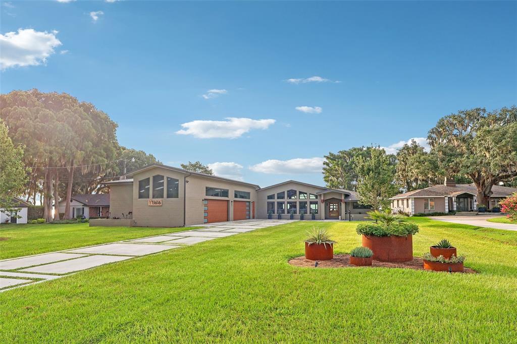 A modern single-story house with a concrete driveway, large lawn, and three rusted metal planters — 1616 LOVES POINT DRIVE, LEESBURG, FL