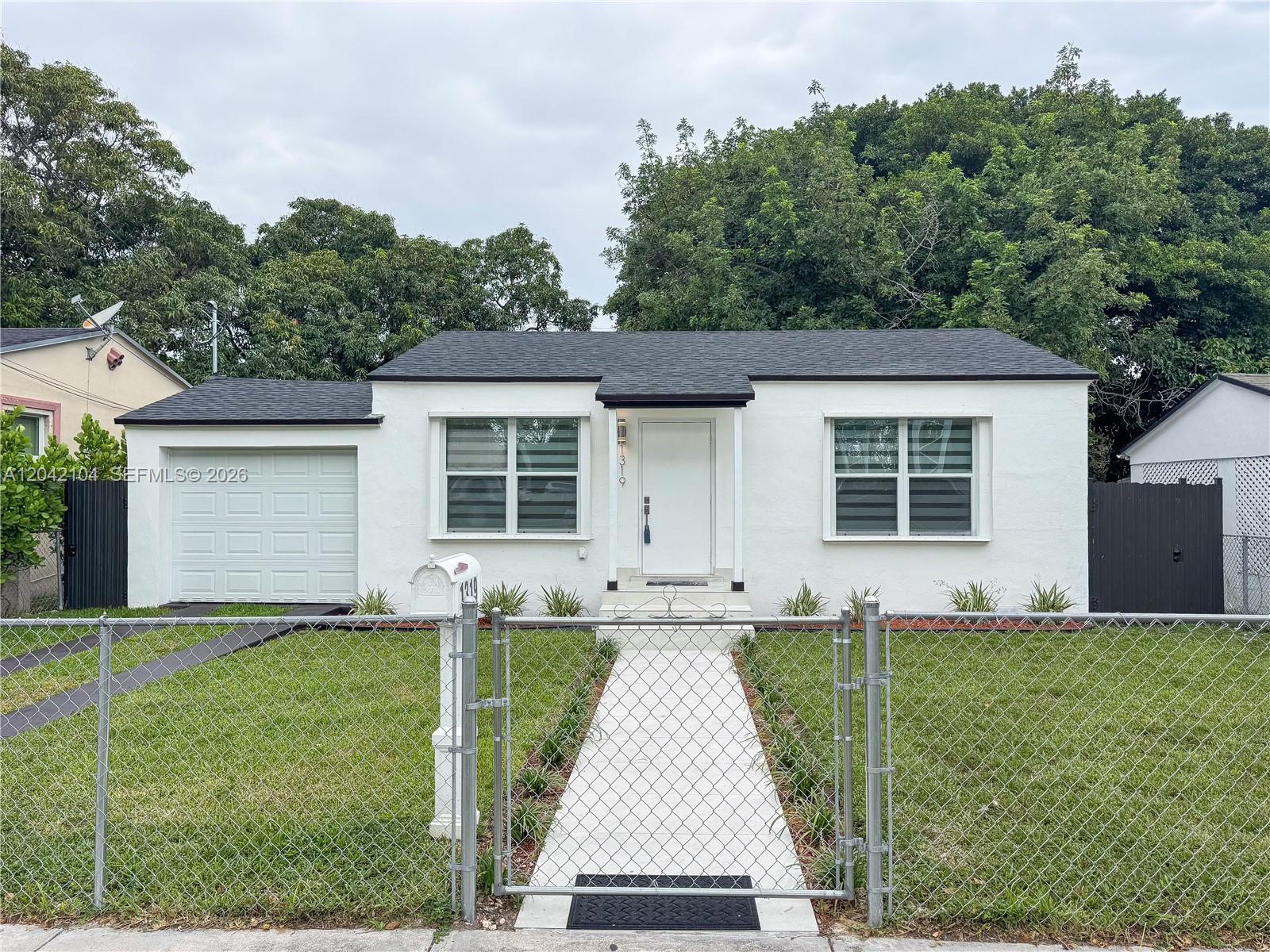 A white single-story house with a black roof and a chain-link fence in front — 1319 NW 40th St, Miami FL 33142, MIAMI, FL