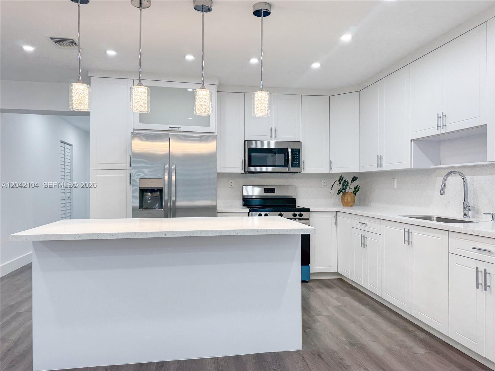 A modern kitchen features white cabinetry, stainless steel appliances, a quartz island, and pendant lighting — 1319 NW 40th St, Miami FL 33142, MIAMI, FL