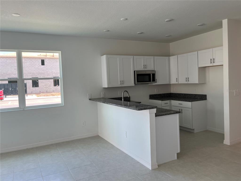 A kitchen features white cabinets, granite countertops, and a breakfast bar overlooking a dining area — 10288 HONEY HAMMOCK WAY, SAN ANTONIO, FL