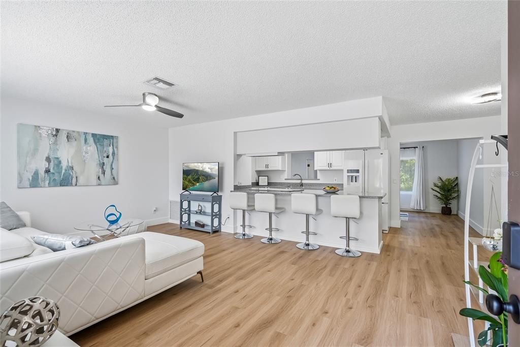 A living room with light wood flooring flows into an open kitchen with bar seating — 1318 S HILLCREST AVENUE, CLEARWATER, FL