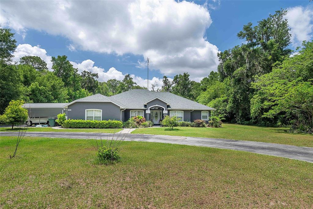 A gray single-story house with a metal carport sits on a large, grassy lot — 50 NE 35TH STREET, OCALA, FL