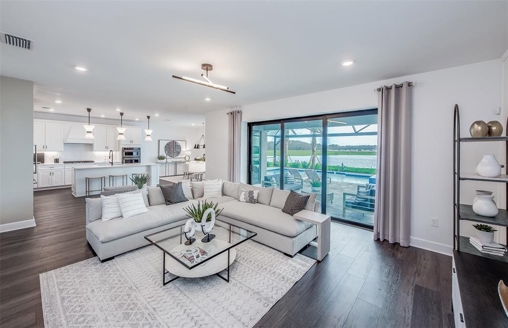 An open-concept living room with a sectional sofa overlooks a patio, pool, and lake — 7457 SUMMER COURT, SARASOTA, FL