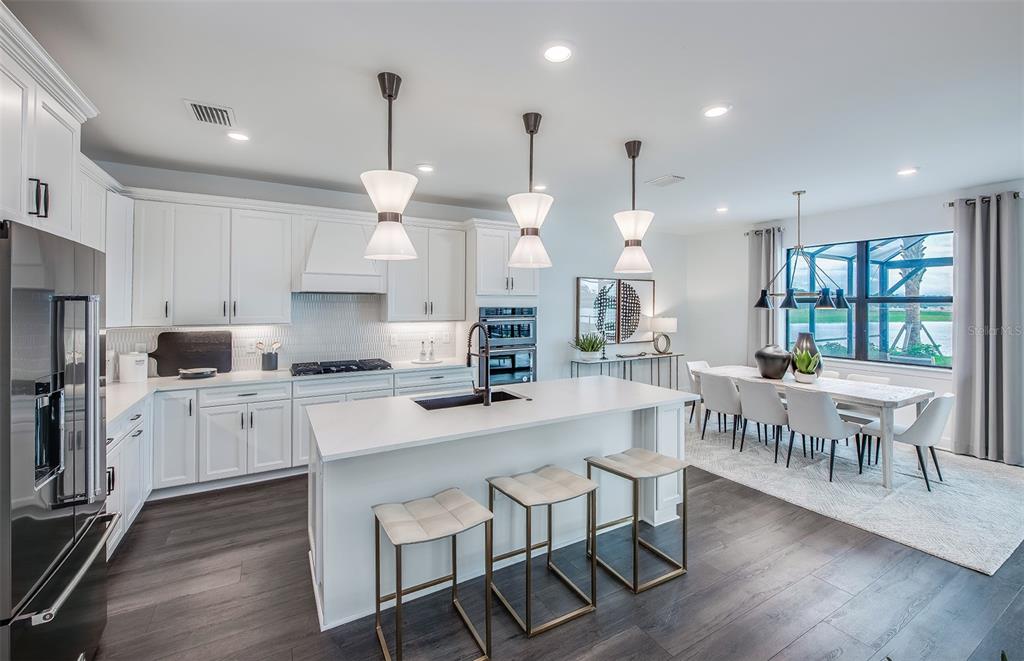 A modern kitchen features white cabinetry, a central island with bar stools, and dining area — 7457 SUMMER COURT, SARASOTA, FL