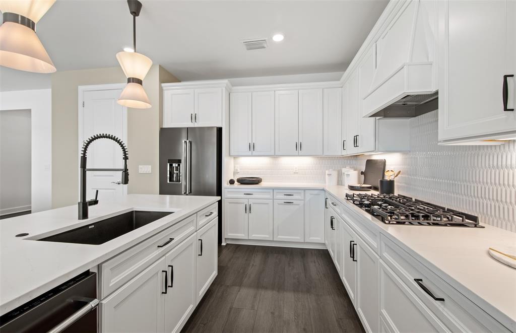 A modern kitchen features white cabinets, a black sink, a gas cooktop, and dark flooring — 7457 SUMMER COURT, SARASOTA, FL