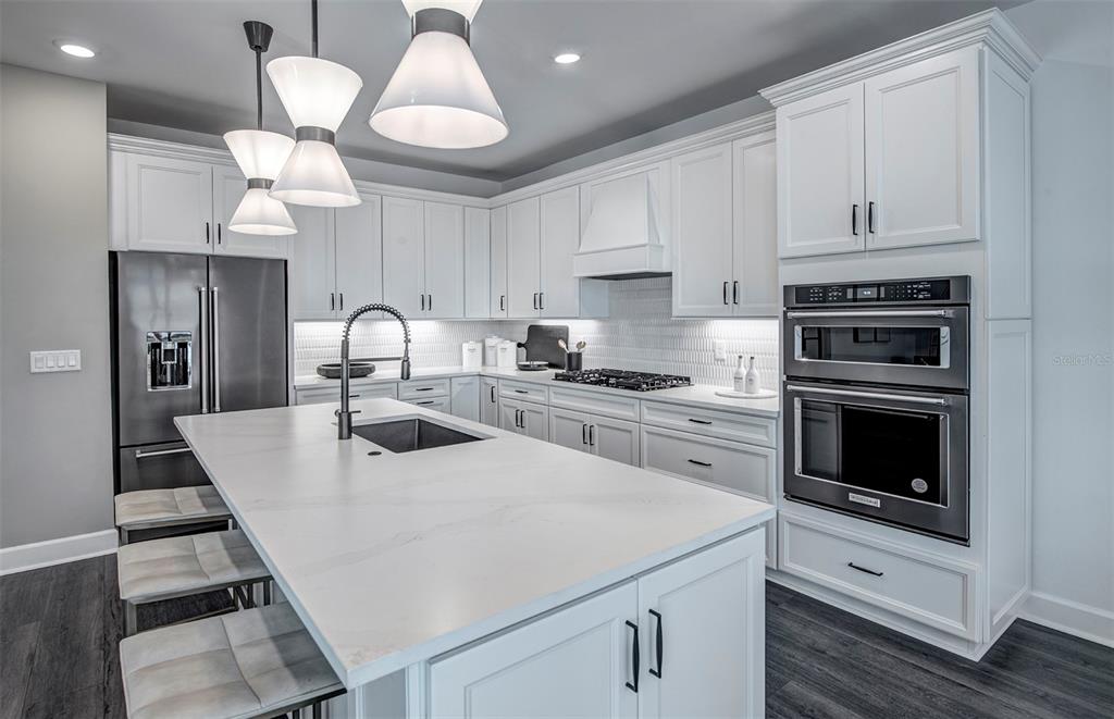 A modern white kitchen features a large island with a sink and stainless steel appliances — 7457 SUMMER COURT, SARASOTA, FL