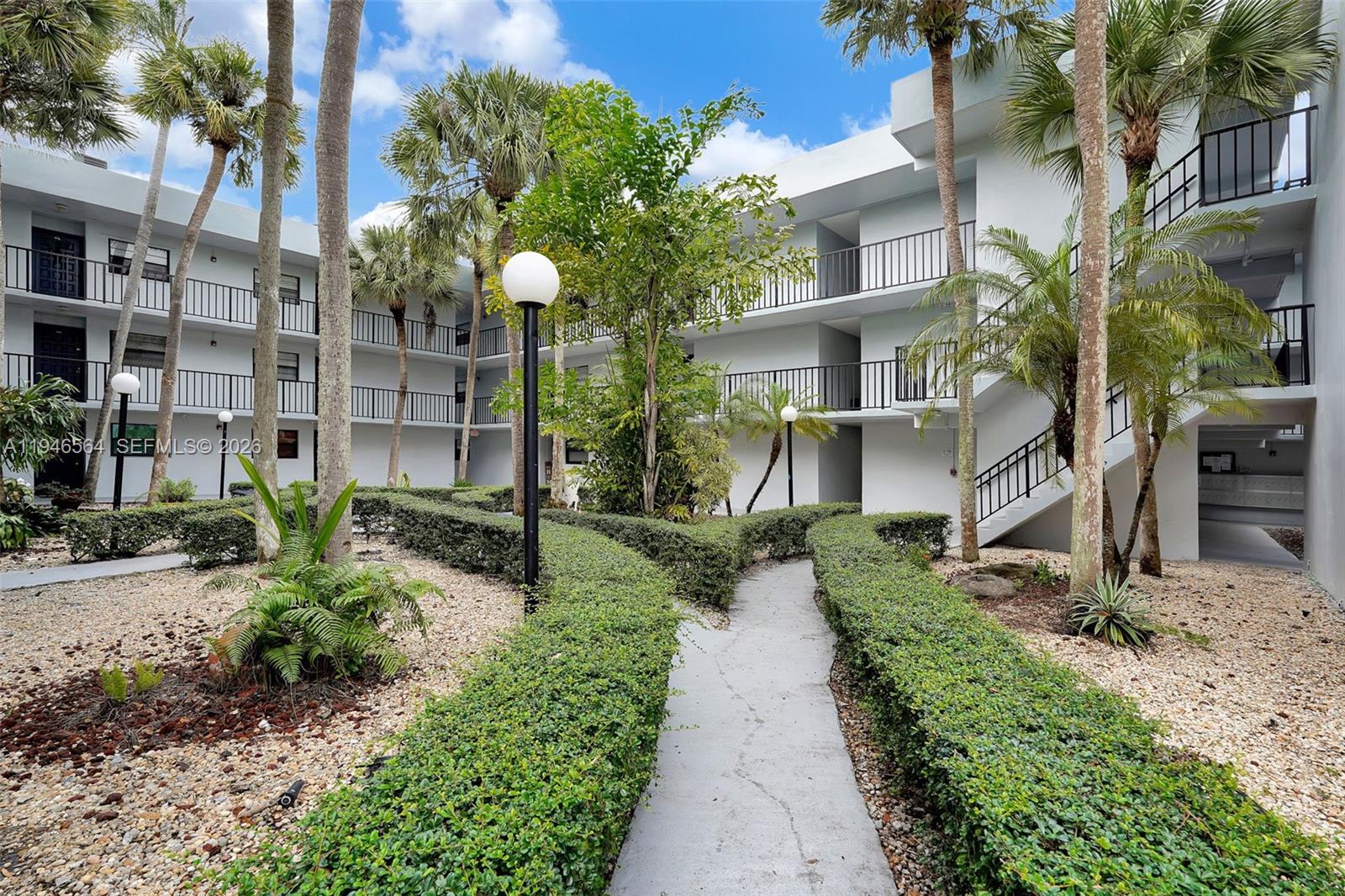 A paved walkway winds through a landscaped courtyard between two multi-story apartment buildings — 10825 SW 112th Ave # 216, Miami FL 33176, MIAMI, FL