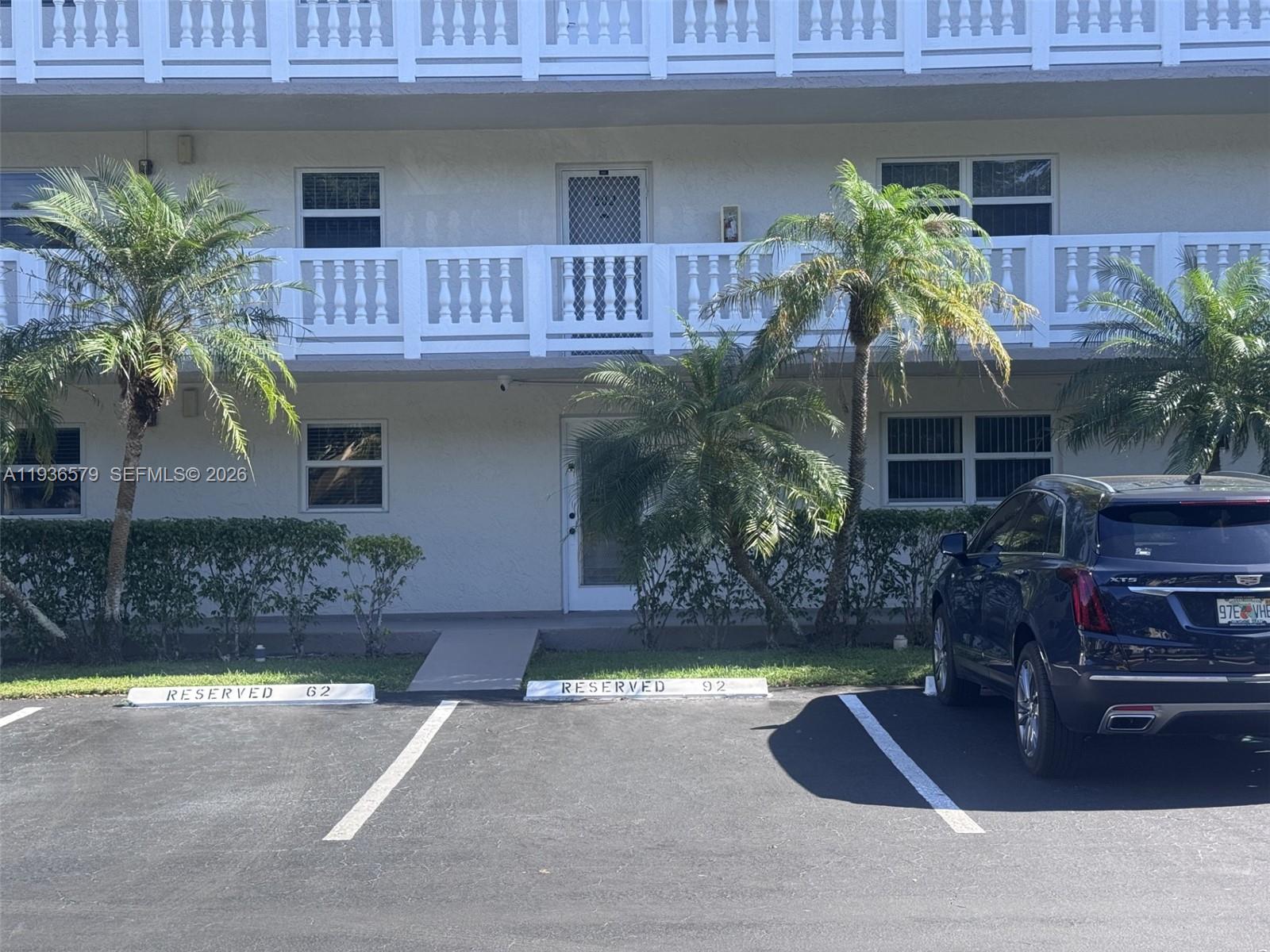 A two-story apartment building exterior features white railings, palm trees, and reserved parking spaces — 1025 SE 3rd Ave # 102, Dania Beach FL 33004, DANIA BEACH, FL