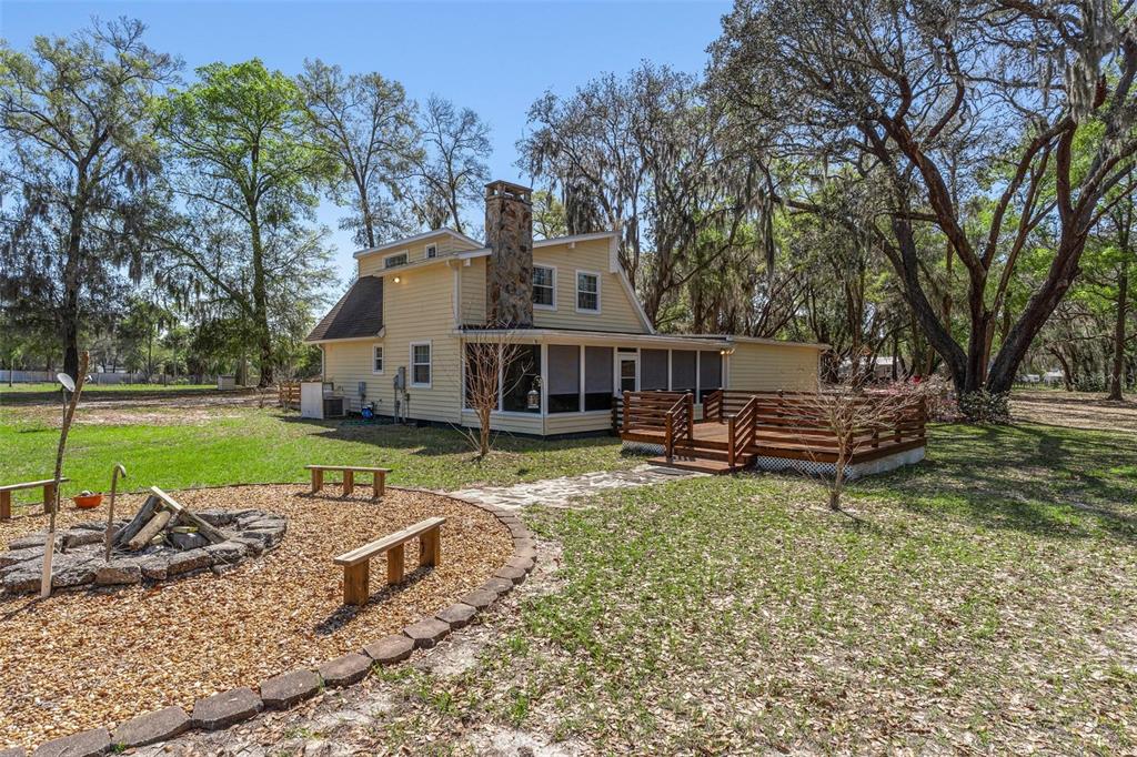 A yellow house with a stone chimney, screened porch, and wooden deck sits in a yard — 2917 LAKE GRIFFIN ROAD, LADY LAKE, FL