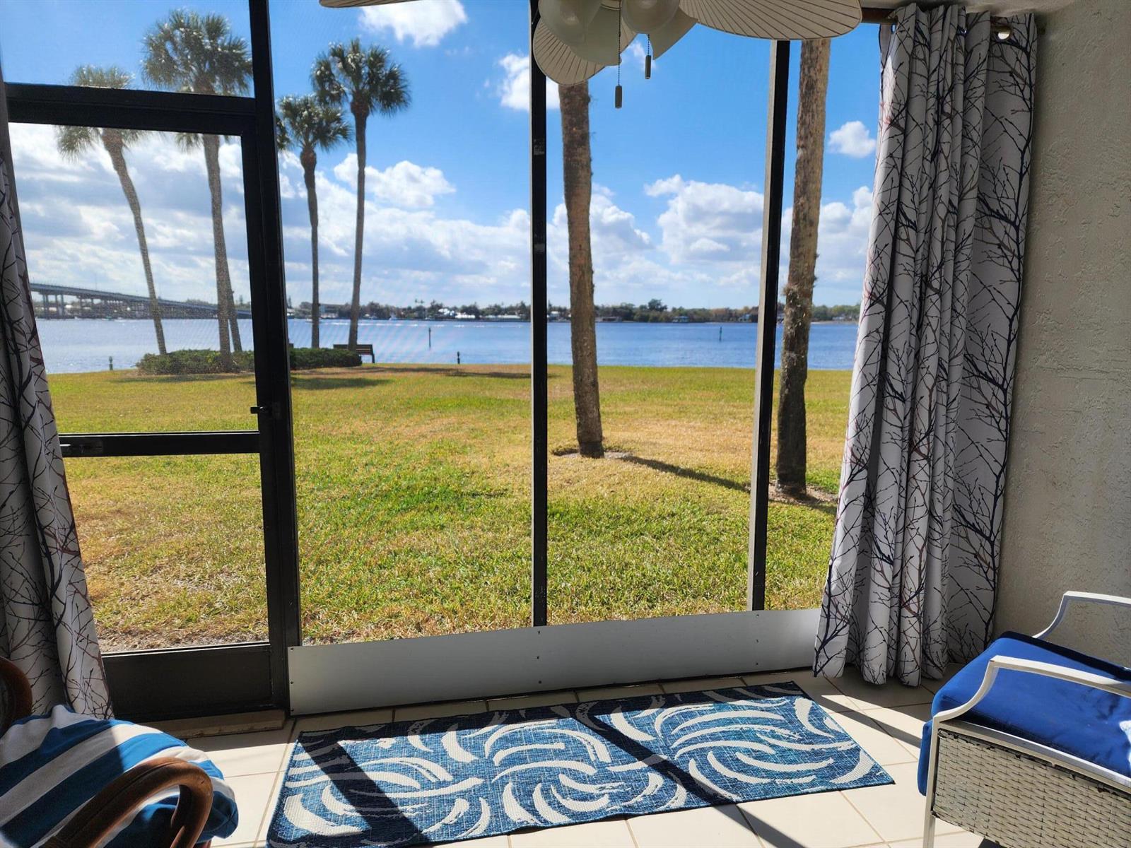 A screened-in porch features a blue patterned rug, patio furniture, and a waterfront view — 1950 SW Palm City Road # 102, Stuart FL 34994, STUART, FL