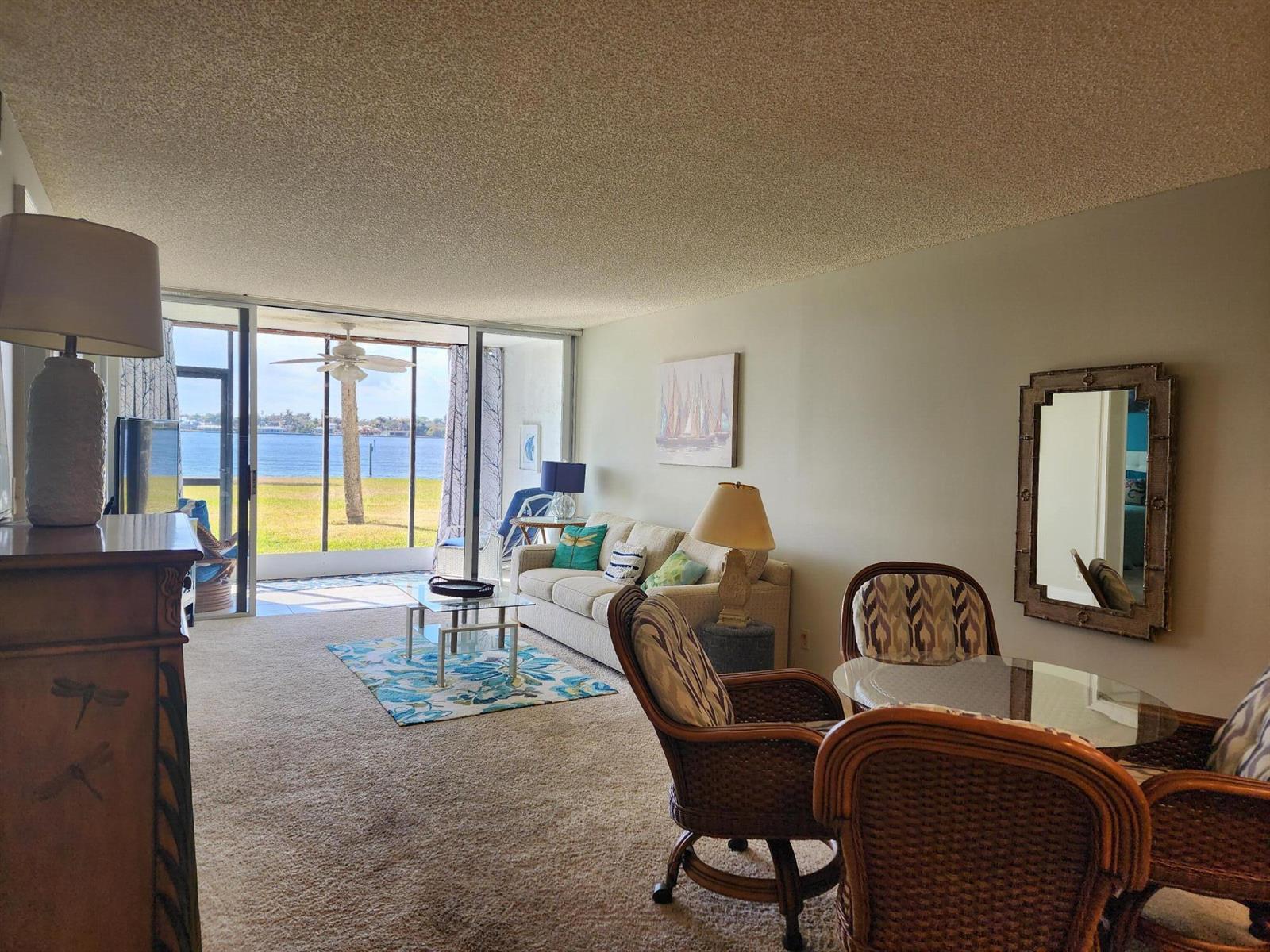 A living and dining area with carpeted floors, wicker chairs, and a view of the water — 1950 SW Palm City Road # 102, Stuart FL 34994, STUART, FL