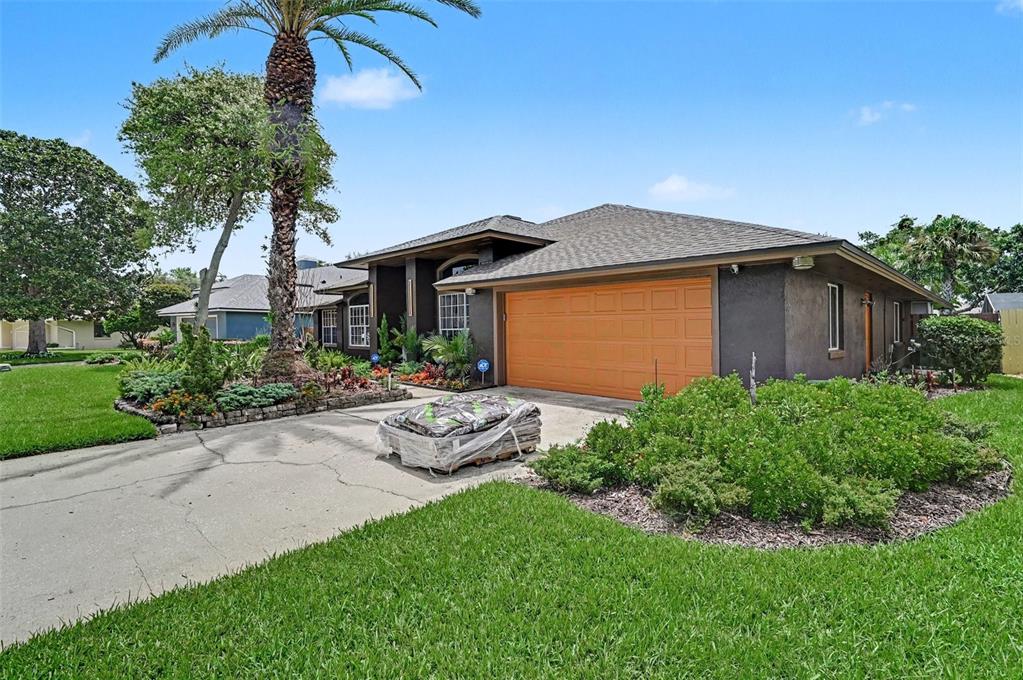 A single-story house with a dark exterior, orange garage door, and a palm tree in front — 455 LONGMEADOW LANE, LONGWOOD, FL
