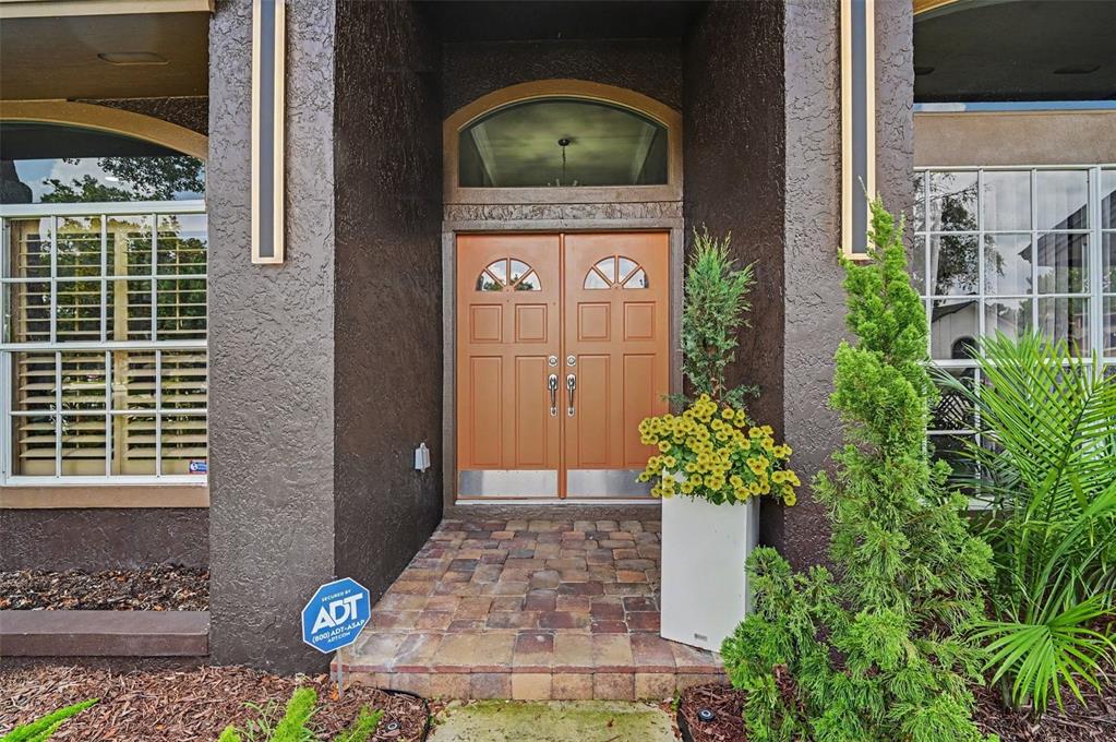 A front entryway features double brown doors, a brick porch, and an ADT security sign — 455 LONGMEADOW LANE, LONGWOOD, FL