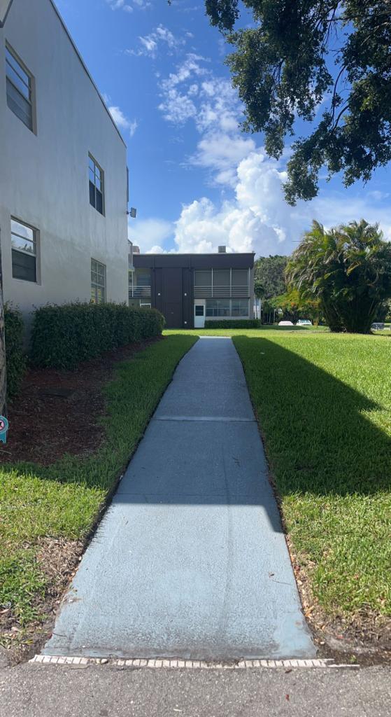 A concrete walkway leads between two apartment buildings toward a grassy area with trees — 816 Normandy Q, Delray Beach FL 33484, DELRAY BEACH, FL