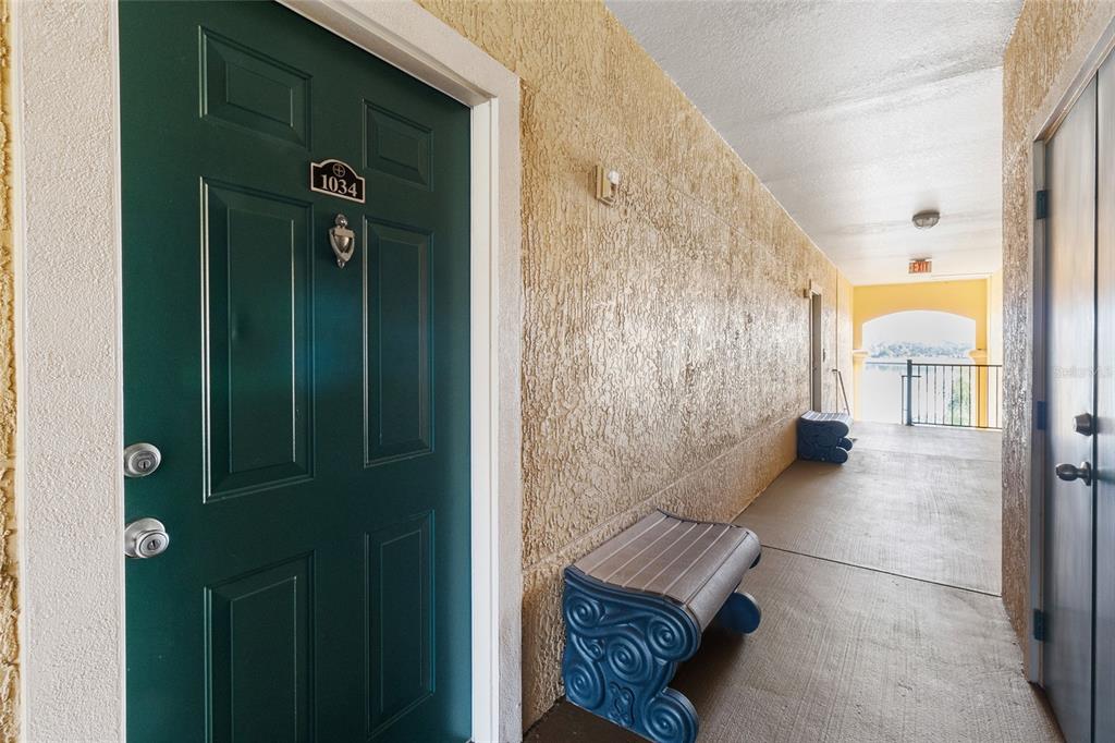 A green door with a brass knocker stands in a hallway with textured beige walls — 2739 VIA CAPRI UNIT 1034, CLEARWATER, FL