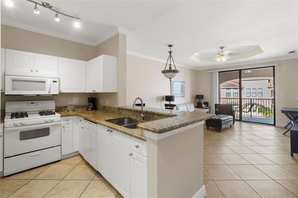 A kitchen with white cabinets and granite countertops opens into a living area with tile floors — 2739 VIA CAPRI UNIT 1034, CLEARWATER, FL