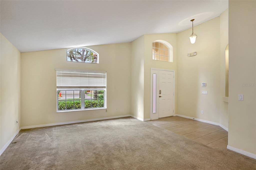 A living room with beige carpet, a vaulted ceiling, a front door, and a window — 1029 ORANGE COSMOS BOULEVARD, DAVENPORT, FL