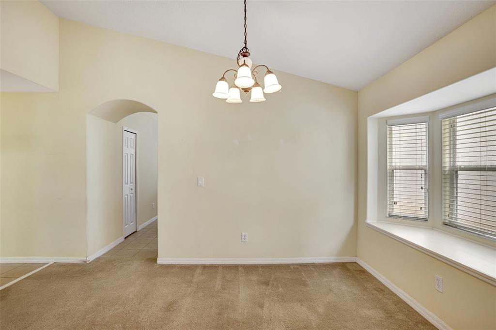 A dining area features beige carpet, a vaulted ceiling, a chandelier, and a bay window — 1029 ORANGE COSMOS BOULEVARD, DAVENPORT, FL
