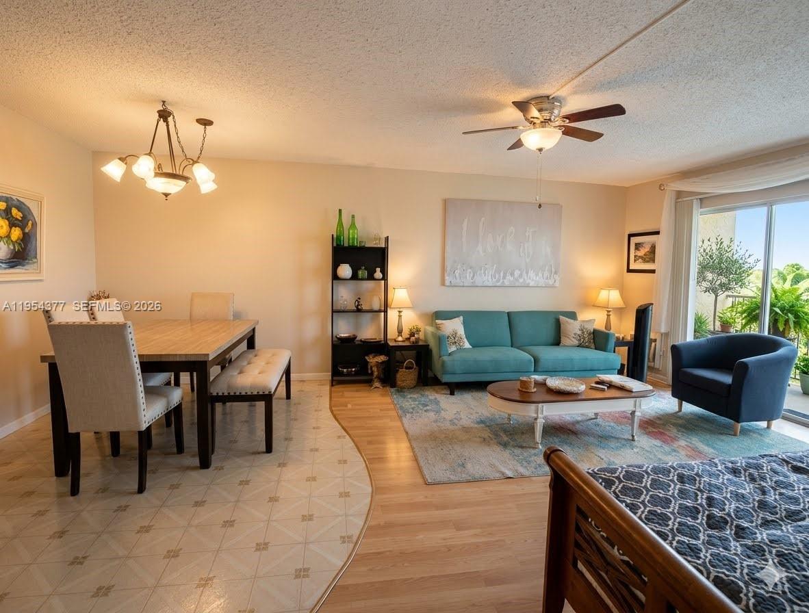 An open-concept living and dining area features tile and wood flooring, a teal sofa, and a balcony — 17001 NE 13th Ave # 314, Miami FL 33162, MIAMI, FL