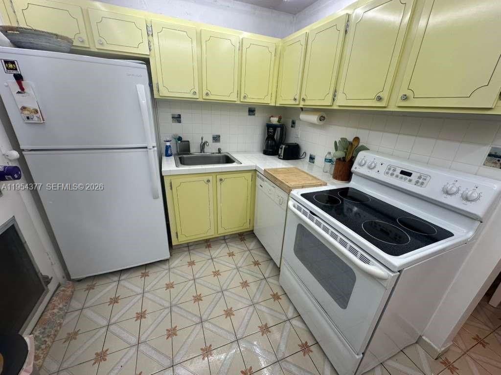 A kitchen features yellow cabinets, white appliances, a tiled backsplash, and patterned floor tiles — 17001 NE 13th Ave # 314, Miami FL 33162, MIAMI, FL