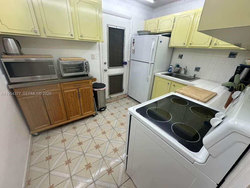 A kitchen features yellow cabinets, a white stove, a refrigerator, and patterned tile flooring — 17001 NE 13th Ave # 314, Miami FL 33162, MIAMI, FL