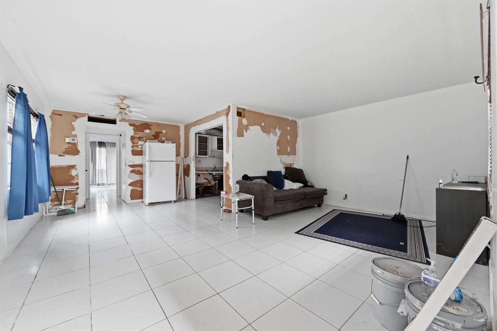 An unfinished living room features white tile floors, exposed drywall, and a brown sofa — 343 Capri # H, Delray Beach FL 33484, DELRAY BEACH, FL