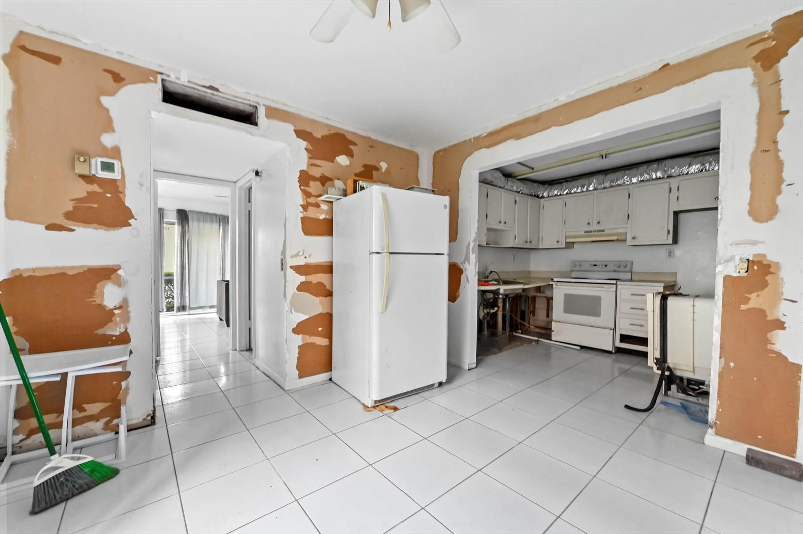 A kitchen and adjacent hallway with white tile floors and walls in need of repair — 343 Capri # H, Delray Beach FL 33484, DELRAY BEACH, FL