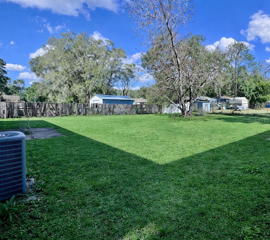 A large, grassy backyard features a wooden fence, several trees, and a small shed — 27319 DALE AVENUE, BROOKSVILLE, FL