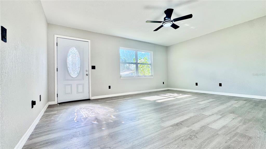 A bright living room features light gray walls, wood-look flooring, and a ceiling fan — 27319 DALE AVENUE, BROOKSVILLE, FL