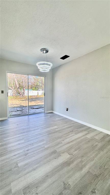 A dining room with gray wood-look flooring, a modern chandelier, and sliding glass patio doors — 27319 DALE AVENUE, BROOKSVILLE, FL