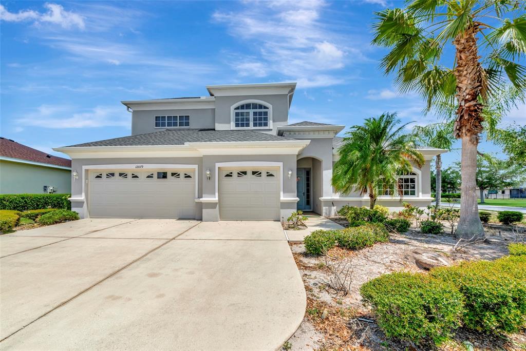 A two-story suburban house with a three-car garage, gray stucco exterior, and a palm tree — 12079 ASTER AVENUE, BRADENTON, FL
