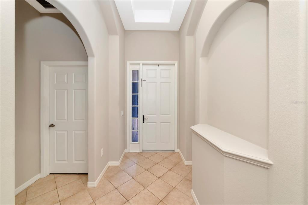 An entryway features a white front door with a sidelight, tiled flooring, and arched walls — 12079 ASTER AVENUE, BRADENTON, FL