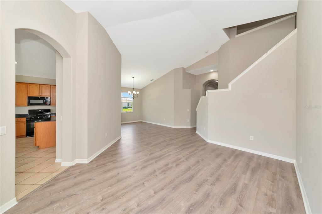 An open-concept living area with light wood-look flooring leads to a kitchen with wooden cabinets — 12079 ASTER AVENUE, BRADENTON, FL