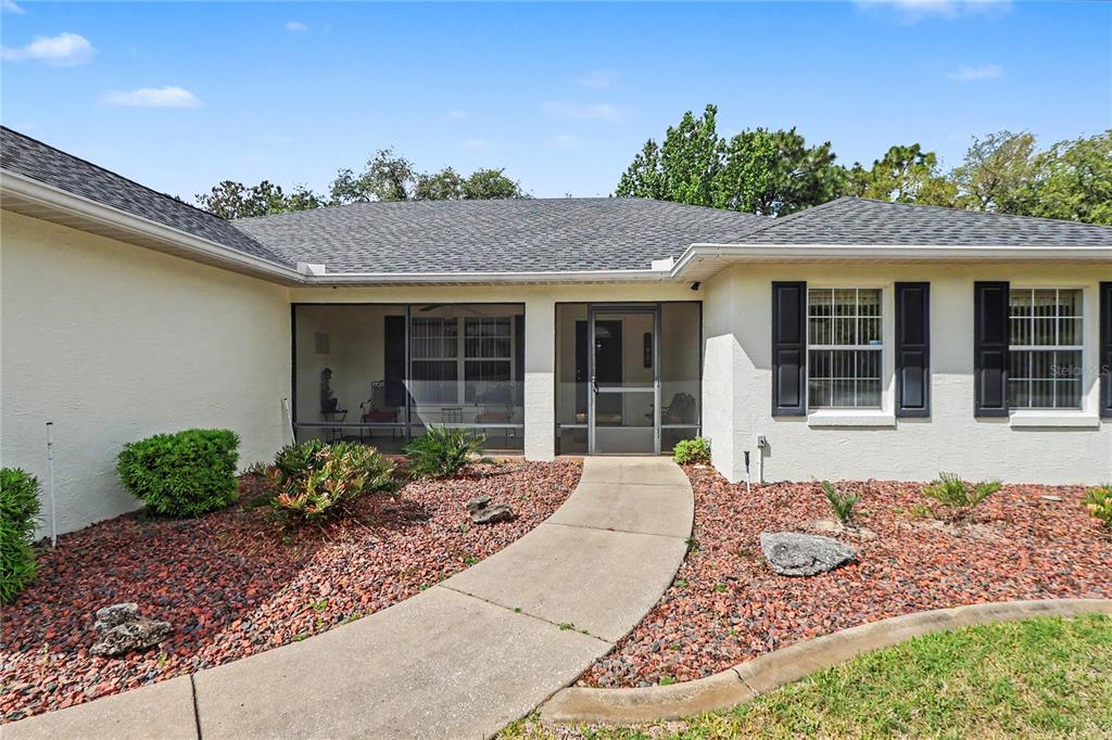 A concrete walkway leads to the screened-in front porch of a single-story stucco house — 10908 SW 53RD CIRCLE, OCALA, FL