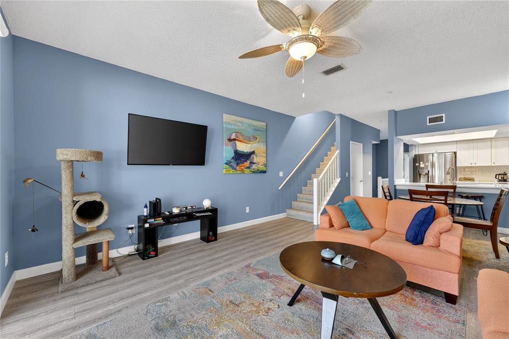 A living room with blue walls, a coral sofa, a ceiling fan, and stairs — 320 ISLAND WAY UNIT 603, CLEARWATER, FL