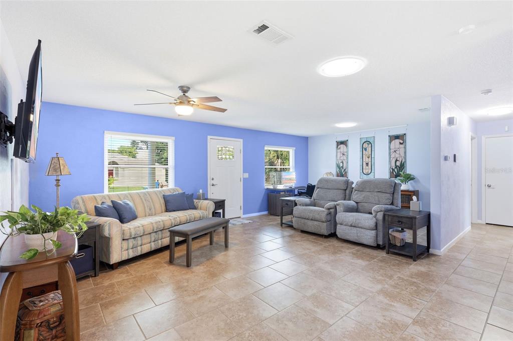 A living room with blue walls, tile flooring, a ceiling fan, and two gray recliners — 411 S BROOKS AVENUE, DELAND, FL