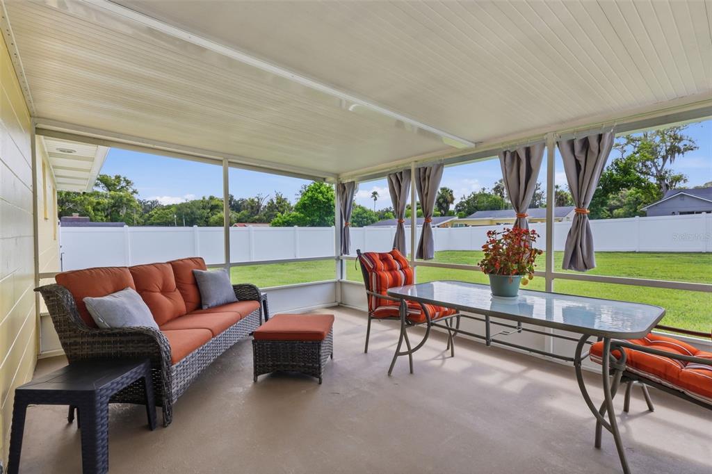 A screened-in patio features a wicker sofa, a glass-top dining table, and a fenced backyard — 411 S BROOKS AVENUE, DELAND, FL