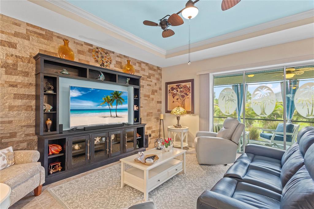 A living room features a stone accent wall, built-in media center, and sliding glass doors — 117 BEAU RIVAGE DRIVE, ROTONDA WEST, FL