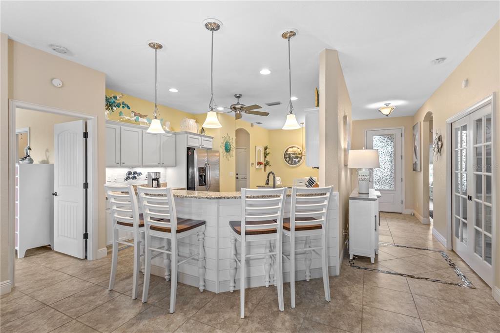 A kitchen features a curved breakfast bar with white stools, light cabinets, and tile flooring — 117 BEAU RIVAGE DRIVE, ROTONDA WEST, FL