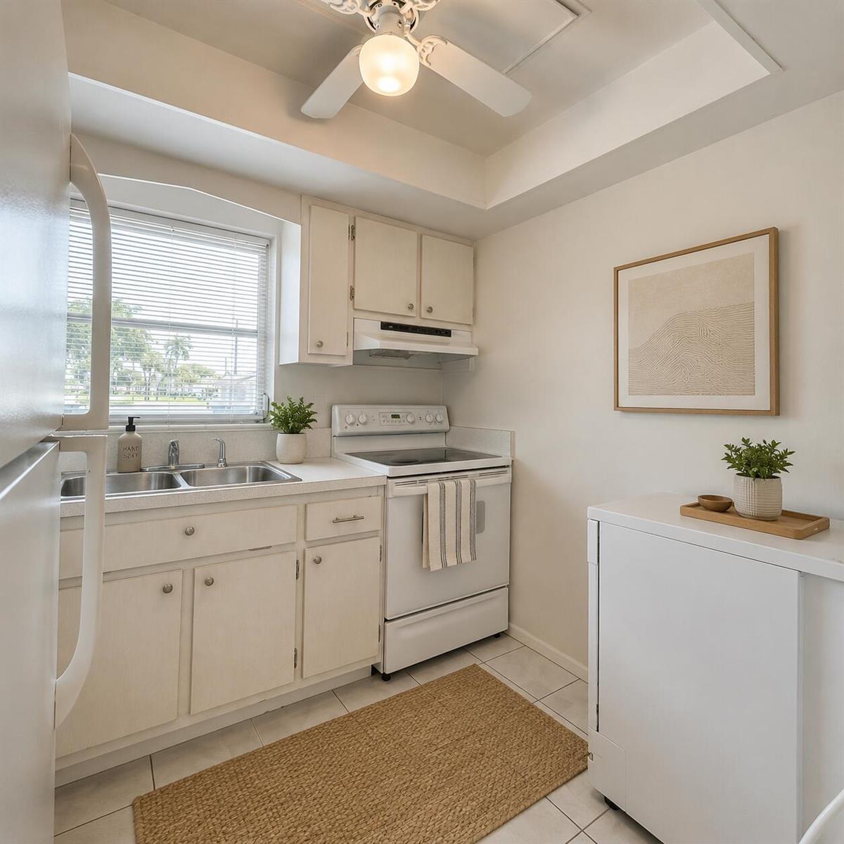 A small kitchen features white cabinets, a white stove, a double sink, and a ceiling fan — 2911 Ashley Dr # J, West Palm Beach FL 33415, WEST PALM BEACH, FL