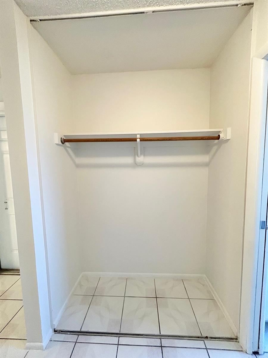 An empty closet with a white shelf, a wooden hanging rod, and tiled flooring — 2911 Ashley Dr # J, West Palm Beach FL 33415, WEST PALM BEACH, FL