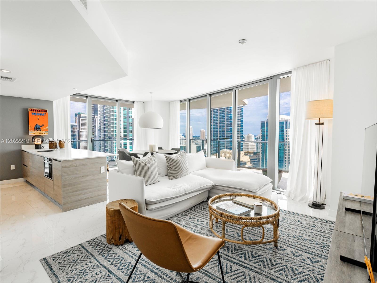 A modern living room with a white sectional, rattan coffee table, and floor-to-ceiling city views — 1300 S Miami Ave # 2901, Miami FL 33130, MIAMI, FL