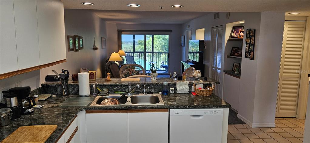 A kitchen with granite countertops and white cabinetry overlooks a living area with balcony access — 2320 TERRA CEIA BAY BOULEVARD UNIT 403, PALMETTO, FL