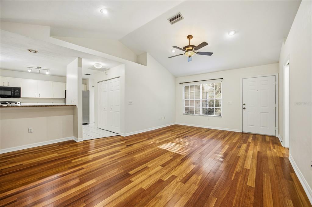 A living room with hardwood floors, a vaulted ceiling, a ceiling fan, and an adjacent kitchen — 4511 NW 35TH STREET, GAINESVILLE, FL